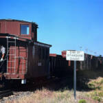 blue sky in background, train next to sign in foreground