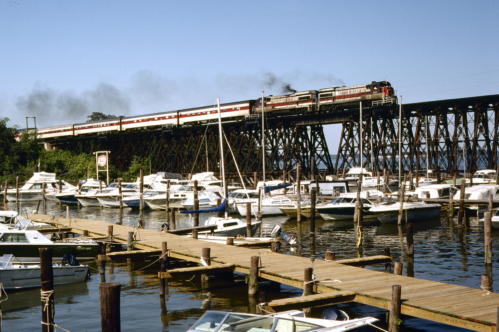 long train on bridge with ships below