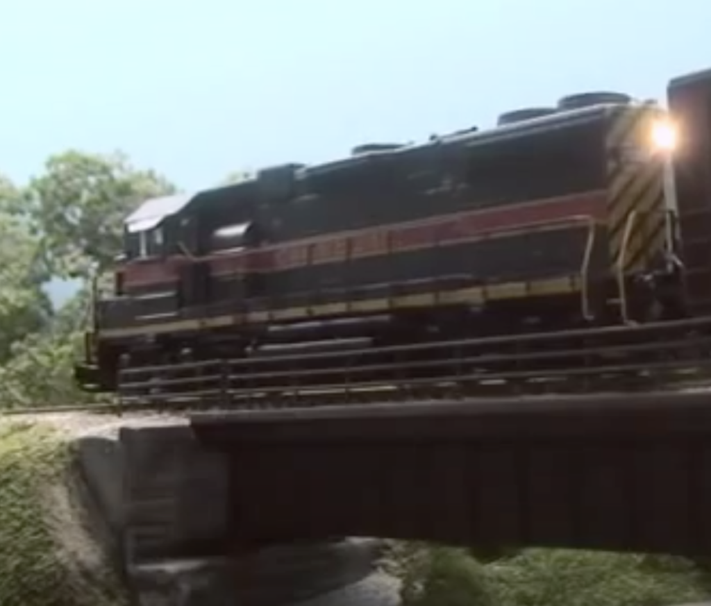 Oblique rear view of a black model diesel locomotive on a bridge.