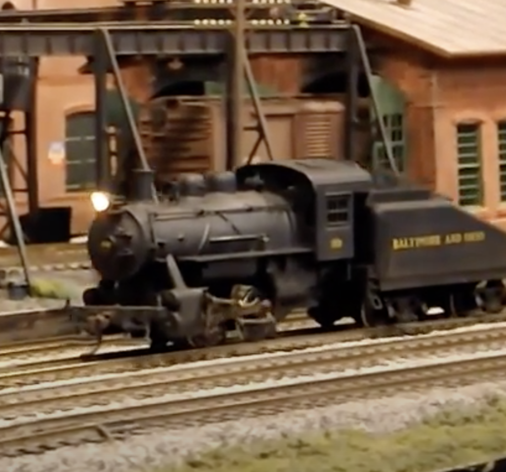 0-4-0 model steam locomotive shown in a rail yard.