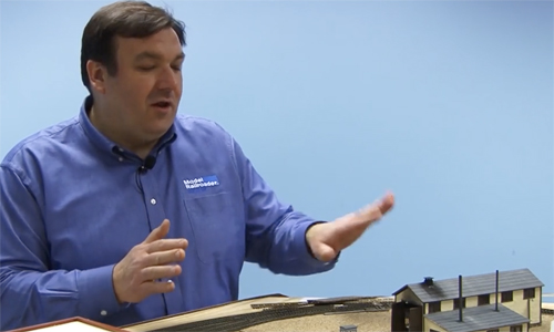 Man gesturing over a model train layout.