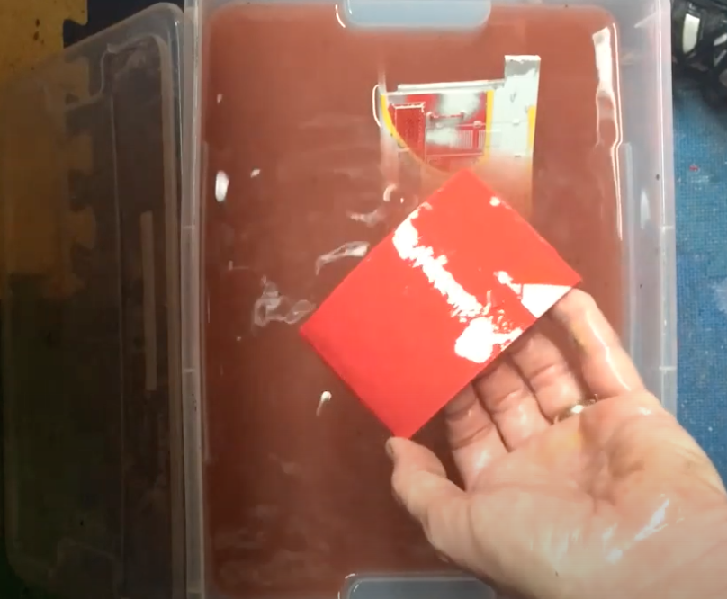 A hand holding a plastic locomotive part in a liquid bath.