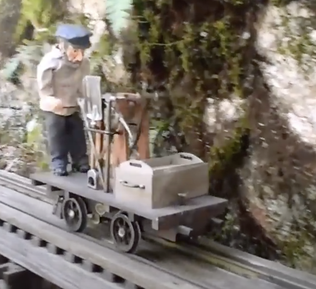 Garden scale figure operating a similar sized hand car.