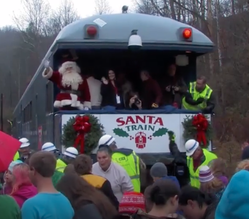Crowds surrounds back of train platform holding Santa Claus.