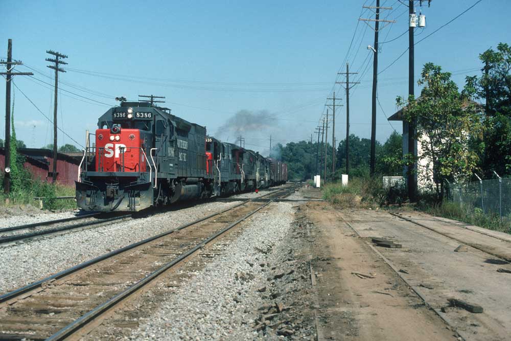 Gray and red diesel locomotives pull freight train by interlocking tower