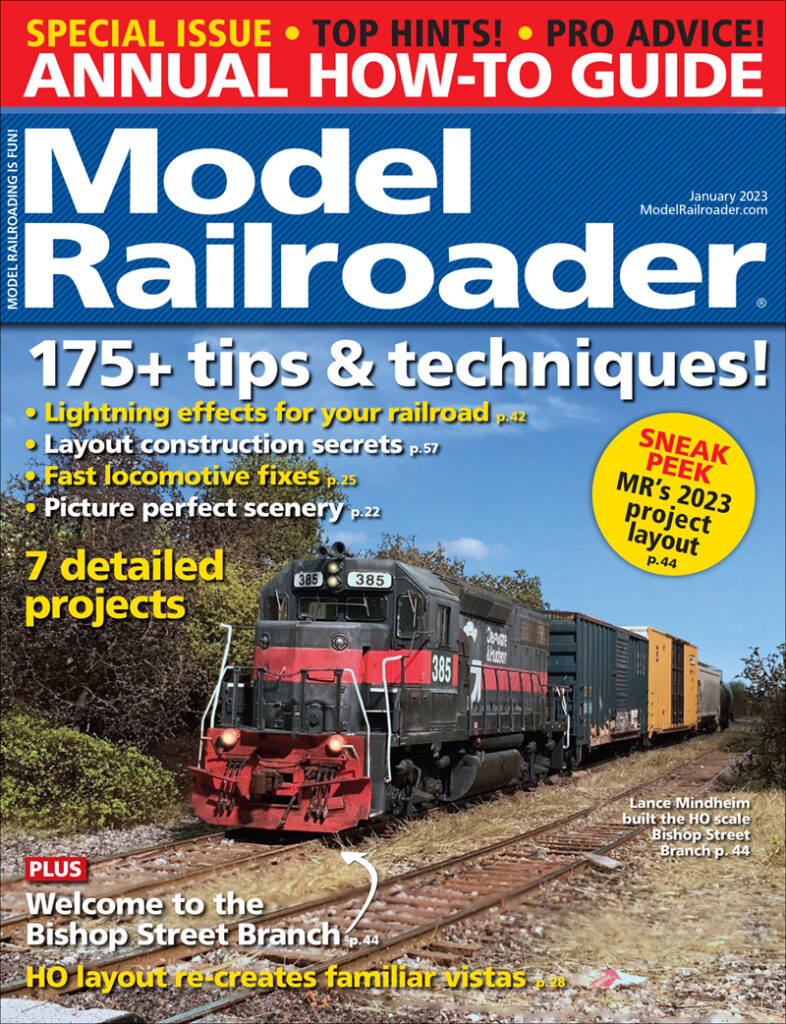 A black and red locomotive runs through a forested section of track against a blue background