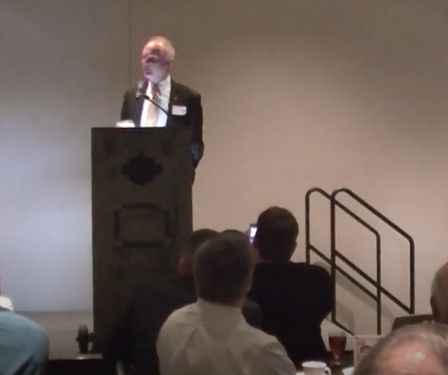 Man standing at podium in front of crowd.