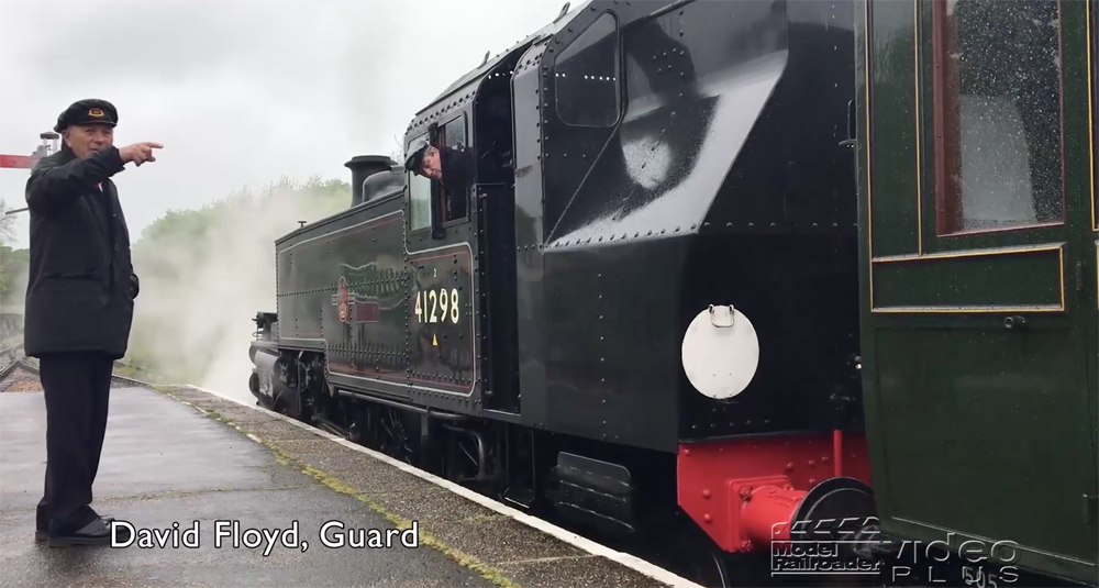 A man beside a steam locomotive conducting operations from a platform in England.