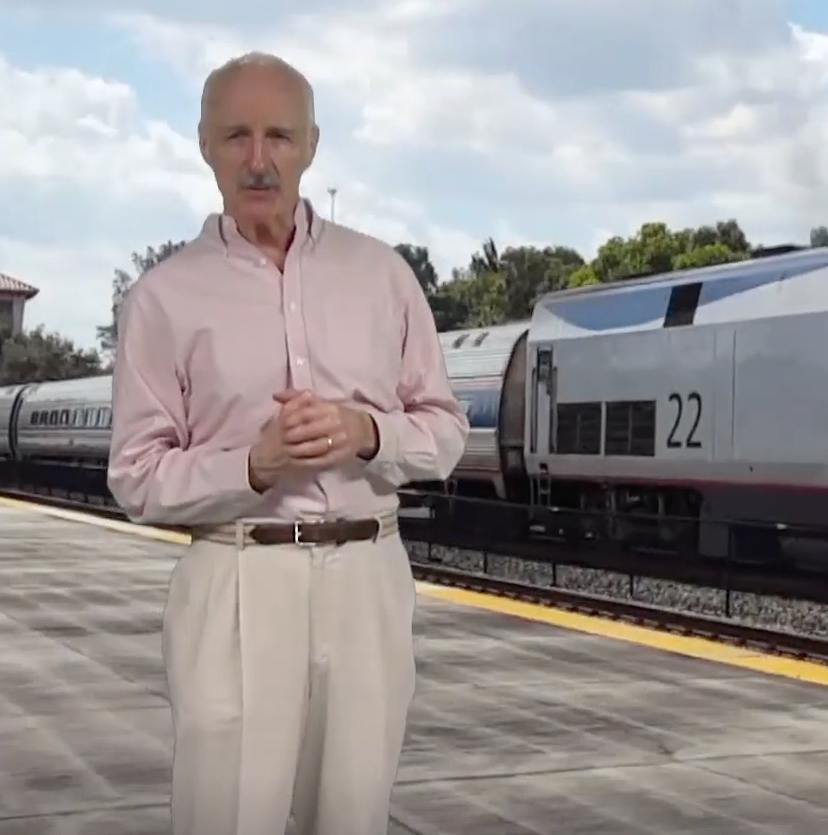 Man standing in foreground with passenger train in background.