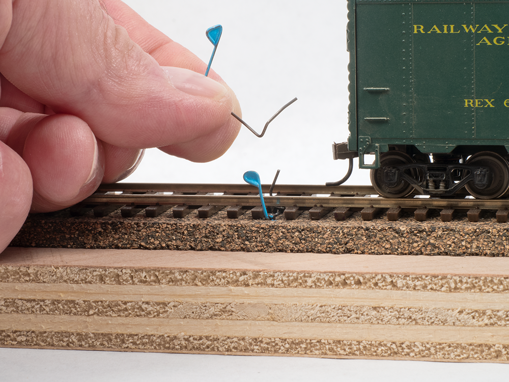 A hand installing bent paperclips into tracks on a model railroad