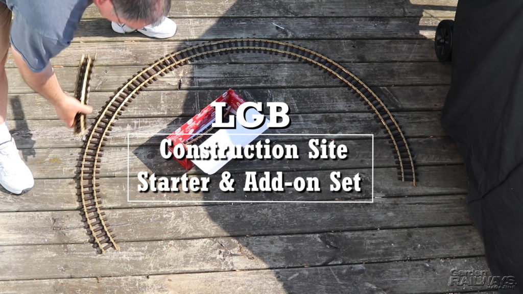 Man bent over and assembling large-scale circle of track encircling track box on a faded wooden deck. White-letter text overlays the scene.