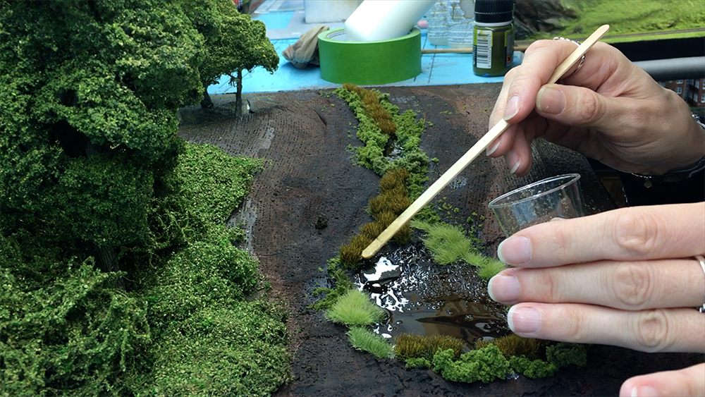 Someone applying glue to place down grass on a layout