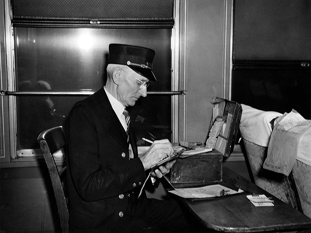 a black and white photo of a conductor writing in a notepad at his desk