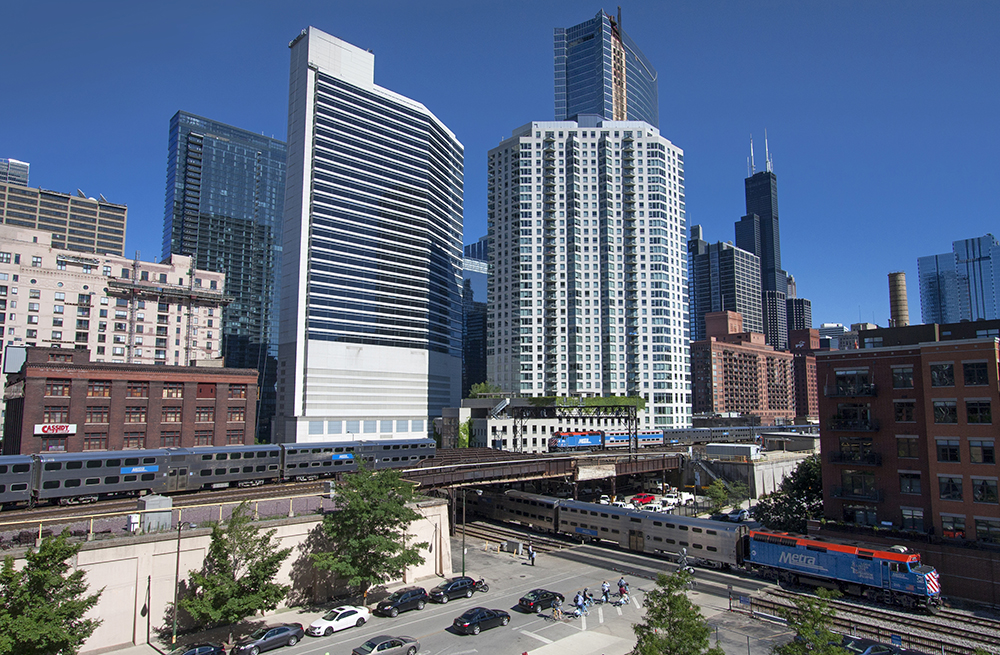 A major metropolitan city with a couple of diesel trains by tall buildings