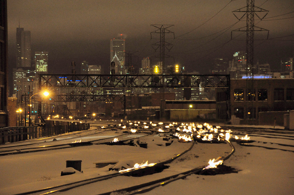 Snowy tracks with little flames on them with a city in the background