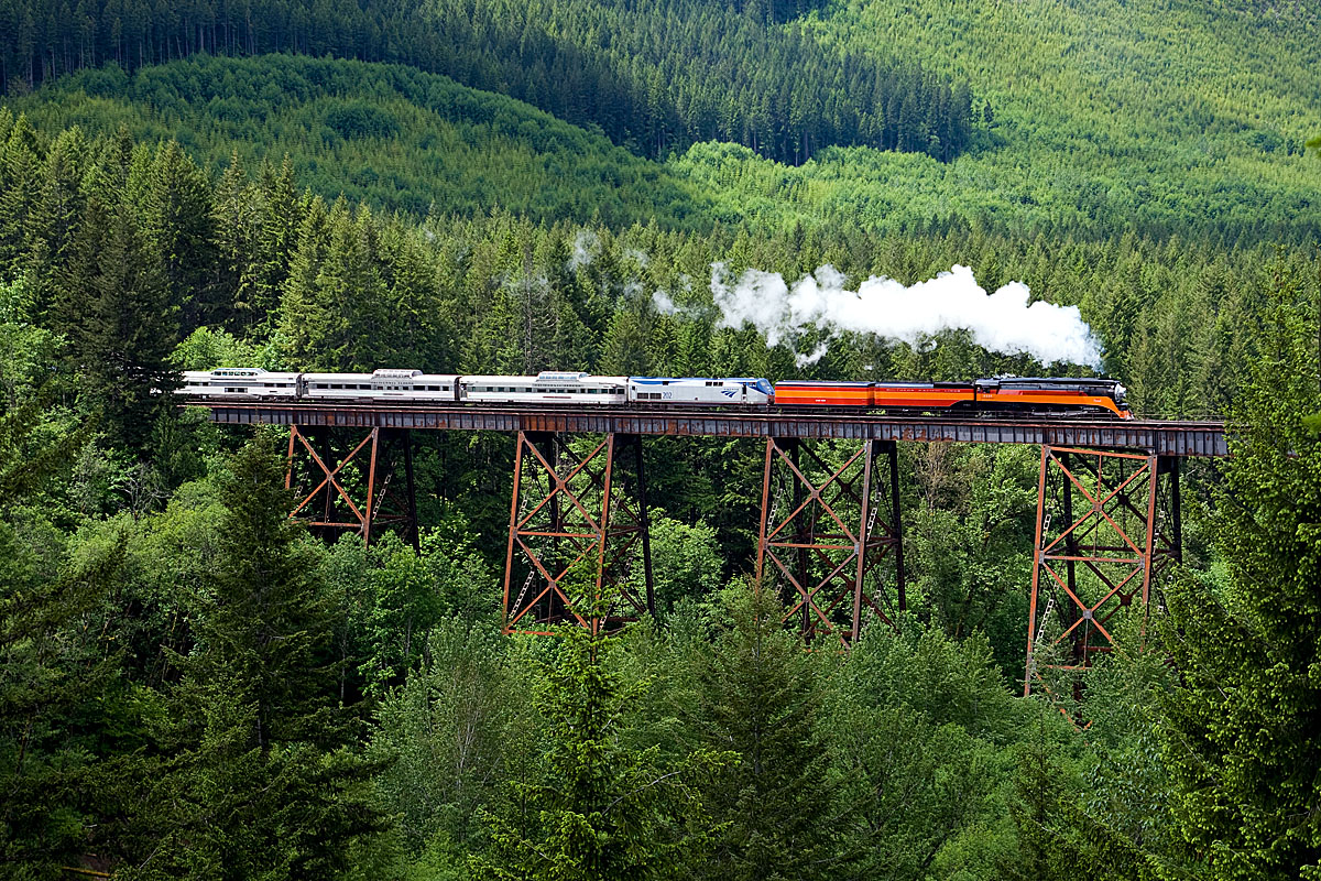 Steam-powered excursion train crosses a bridge in the mountains.