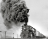 A train coming down the tracks with big black smoke coming out of its chimney