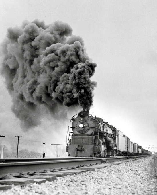 A train coming down the tracks with big black smoke coming out of its chimney