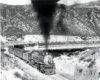 A black and white photo of locomotive 2-10-2 on the tracks with black smoke coming out of its chimney as it turns