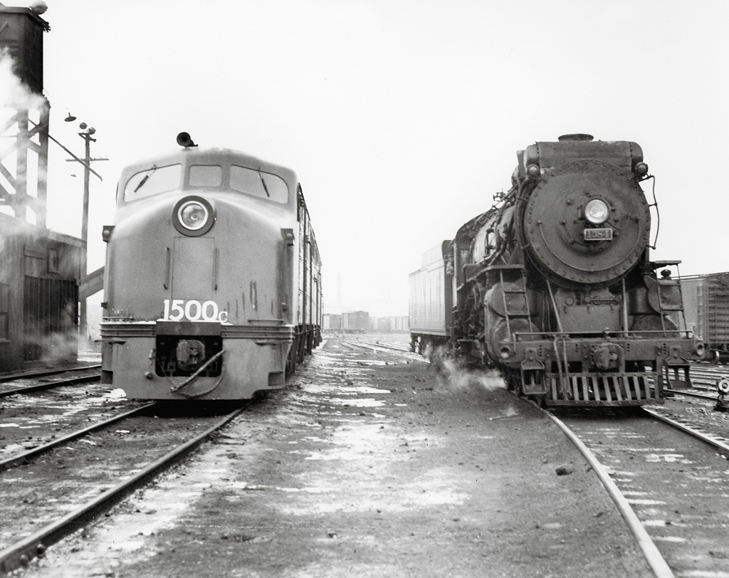 Steam locomotive and diesel locomotive side by side in a rail yard.