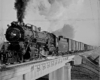 Smoking steam Missouri Pacific locomotives with freight train on bridge
