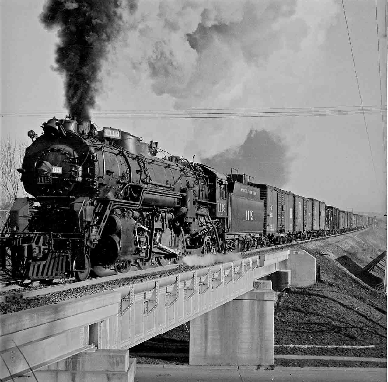 Steam locomotive hauling train over a bridge.