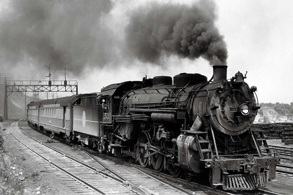 Smoking steam locomotive with passenger train under signal bridge