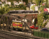 A model 2-8-8-4 steam locomotive pulls a train over a brick viaduct in the background of a verdant city scene.