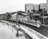 Streamlined passenger train below buildings along river