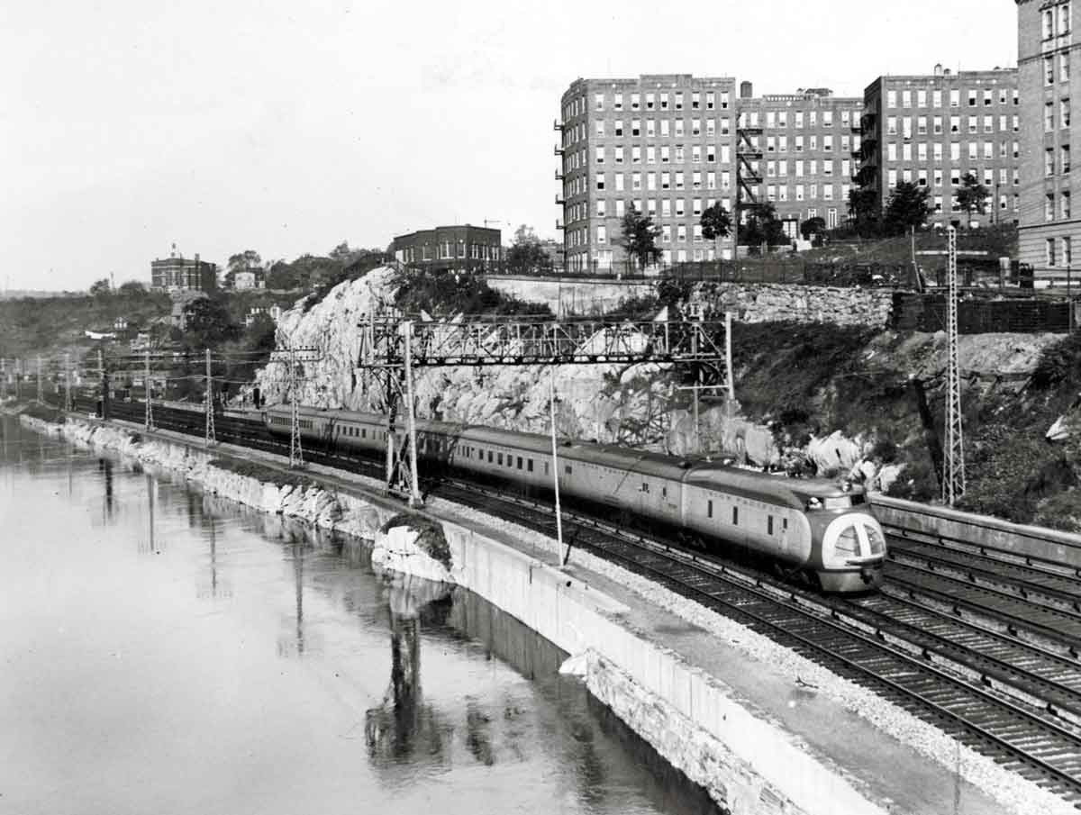 Streamlined passenger train below buildings along river