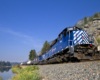 A blue train passing by a body of water