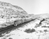 A black and white photo of a FP45 locomotive on the tracks moving through the mountains 