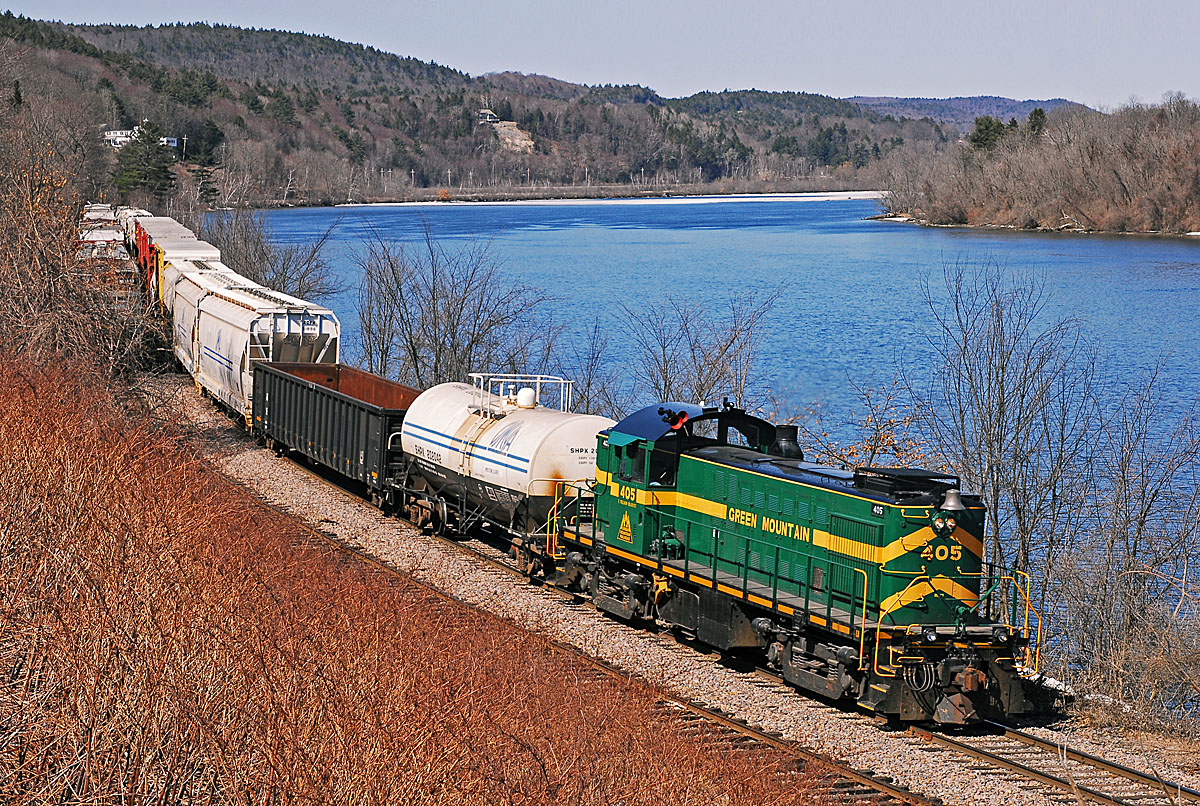 A train turning a corner next to a body of water