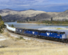 A blue train turning a corner next to a body of water