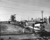 A black and white photo of Texas & Pacific F7A 1553 locomotive on the tracks with a city skyline in the background