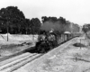 A black and white photo of locomotive 4-8-2 3711 on the tracks passing a Herpoco sign