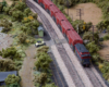 A red express freight train with a caboose on the rear pass through a small town near a river.