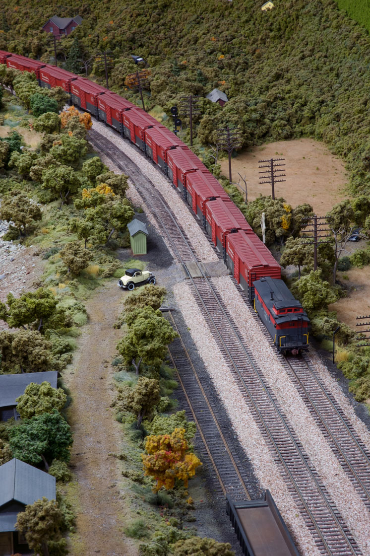 A red express freight train with a caboose on the rear pass through a small town near a river.