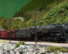 A 4-8-2 steam locomotive leads a stock car train passed several large telephone-telegraph poles.