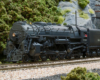 A 4-6-4 steam locomotive leads an express train on a curve exiting a tunnel.