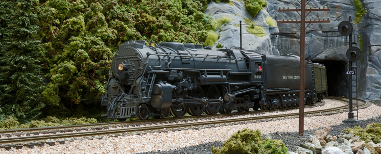A 4-6-4 steam locomotive leads an express train on a curve exiting a tunnel.
