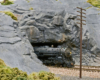 A steam locomotive pokes out of a rock faced tunnel.