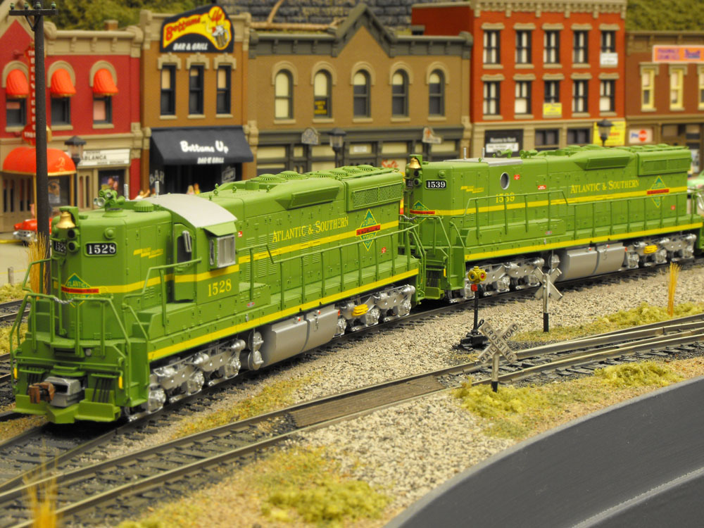 Two model green diesel-electric locomotives in an urban scene.