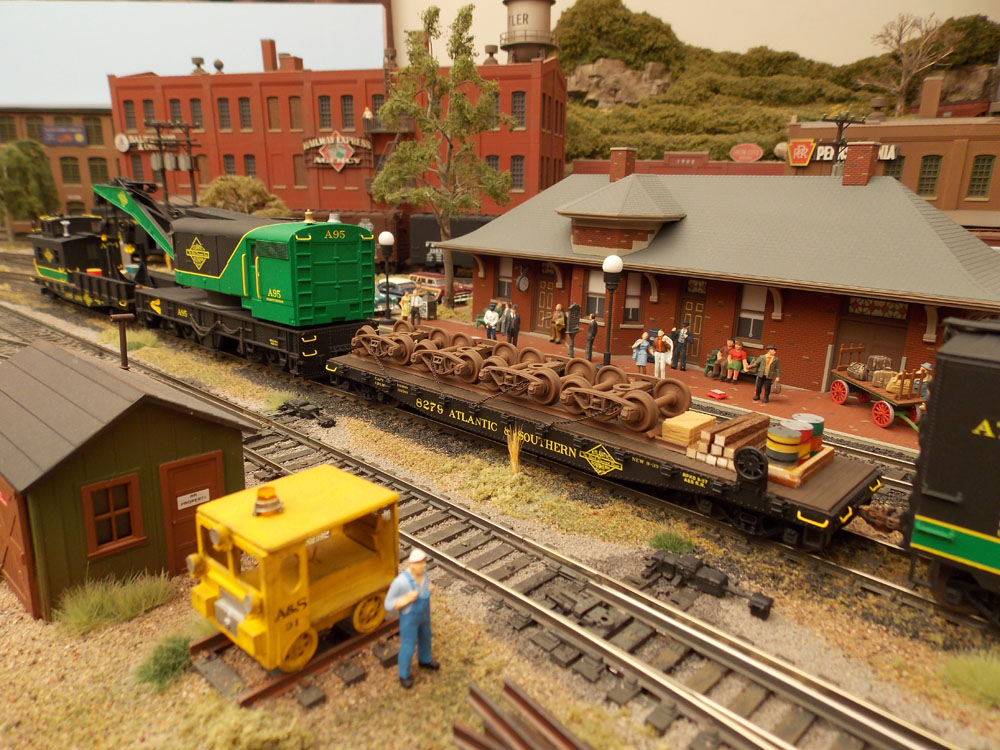 A green-and-black work train in front of a station with passengers. Mostly brick-work downtown.