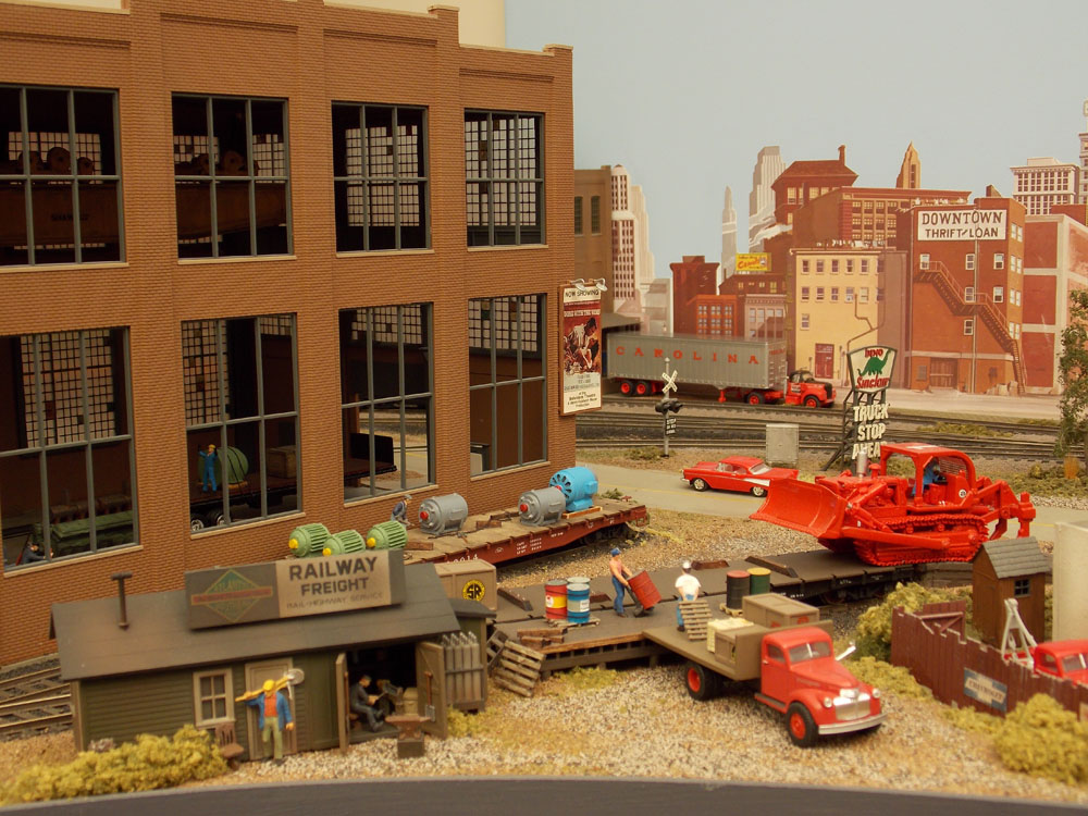 Workers in an industrial scene place "loads" on various flat cars.