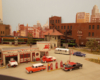 Green and black diesel-electric locomotives haul a freight train in a brickwork industrial scene.