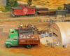 Model trucks loaded with scrap metal near a quonset hut in a rural rail yard.