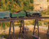 A green steam locomotive hauling a passenger or express train over a trestle in a verdant, arid landscape.