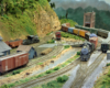 A steam locomotive hauls a freight train through a rural rail yard.
