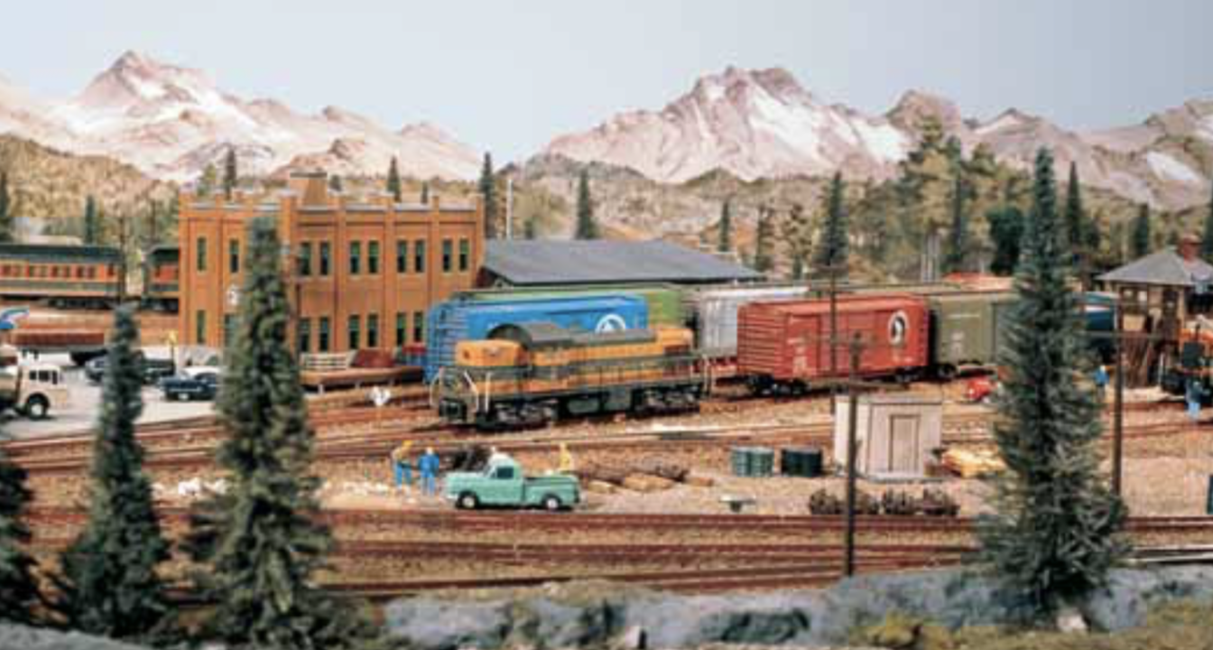 A different view of the layout through evergreen trees and focusing on a Great Northern painted locomotive, likely a GP7.